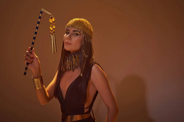 Mujer de moda en mirada egipcia sosteniendo el estilo y mirando a la cámara sobre fondo marrón - foto de stock