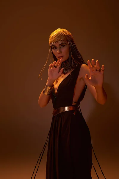 Brünette Frau im ägyptischen Kleid und Blick posiert und schaut in die Kamera isoliert auf braun — Stockfoto