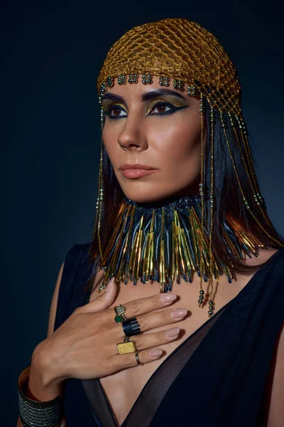 Brunette woman with egyptian makeup and attire posing in headdress on blue background — Stock Photo