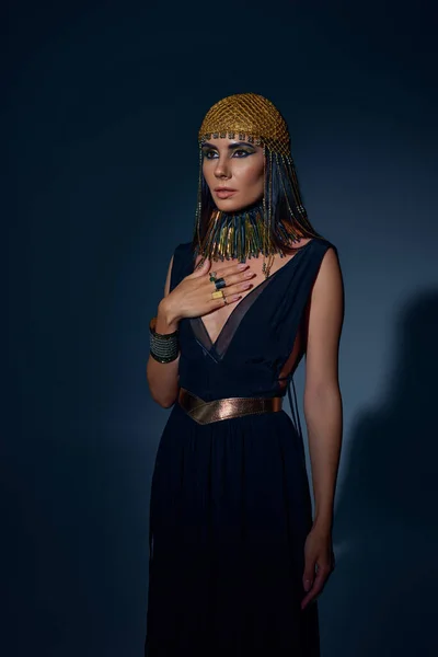 Mulher elegante em cobertura para a cabeça egípcia e colar posando enquanto em pé sobre fundo azul — Fotografia de Stock