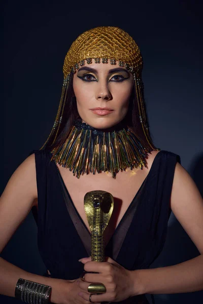 Portrait of woman in egyptian look and headdress holding crook in snake shape on blue background — Stock Photo