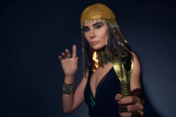 Blurred woman in egyptian look holding crook in snake shape while standing on blue background — Stock Photo