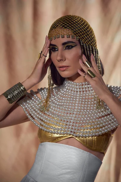 Портрет брюнетки в єгипетському костюмі та перлинному намисті, що стоїть на абстрактному тлі — стокове фото