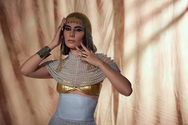 Stilvolle Frau mit ägyptischem Kopfschmuck und Perlenkleid blickt in die Kamera auf abstraktem Hintergrund — Stockfoto