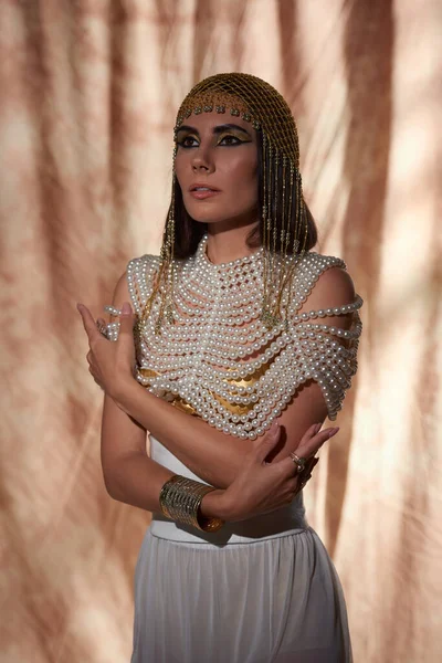 Retrato de mujer morena en top de perlas y mirada egipcia posando sobre fondo abstracto - foto de stock