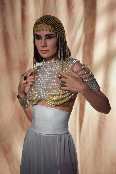 Mujer en tocado egipcio tradicional, top de perlas y look posando sobre fondo abstracto - foto de stock