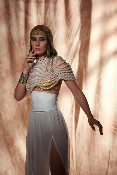 Елегантна жінка в єгипетському головний убір і перлина зверху дивиться на камеру на абстрактному фоні — стокове фото