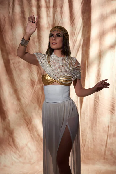 Elegante donna in look egiziano e trucco in posa mentre in piedi su sfondo astratto — Foto stock