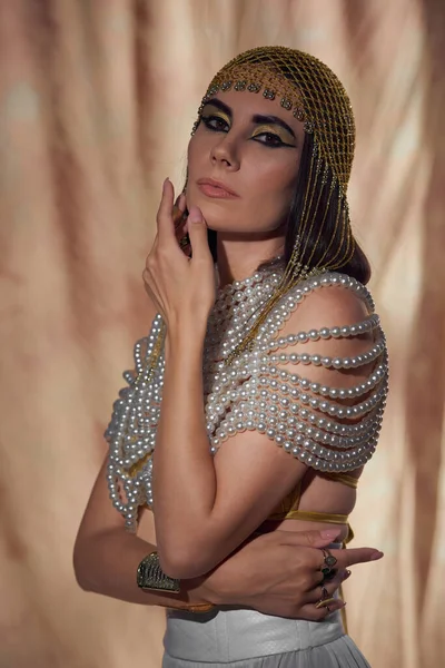Mulher morena em cobertura para a cabeça egípcia, top pérola e maquiagem posando em fundo abstrato — Fotografia de Stock