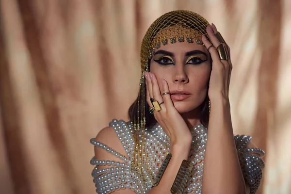Porträt einer Frau mit ägyptischem Kopfschmuck und Perlenkette, die das Gesicht auf abstraktem Hintergrund berührt — Stockfoto