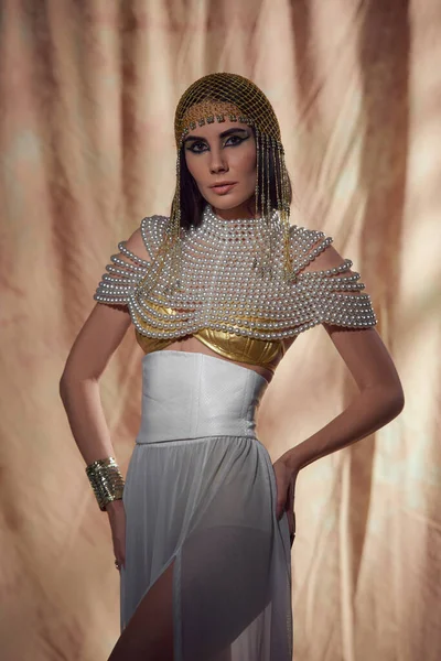 Модная женщина в египетском головном уборе и костюме позирует и стоит на абстрактном фоне — стоковое фото