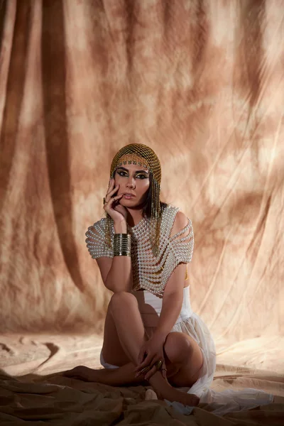 Mulher elegante em cobertura para a cabeça egípcia e top pérola olhando para a câmera em fundo abstrato — Fotografia de Stock