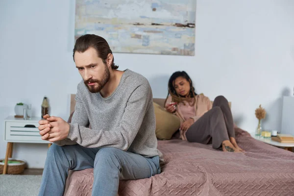 Uomo triste seduto sul letto, sensazione di stress, donna afro-americana con test di gravidanza, decisione — Foto stock