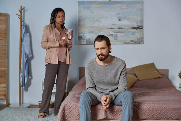 African american woman holding pills and glass of water, looking at stressed man, abortion concept — Stock Photo
