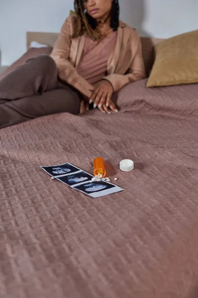 Противозачаточные таблетки возле ультразвукового фото, африканская американка на кровати, принятие решения, стресс — стоковое фото
