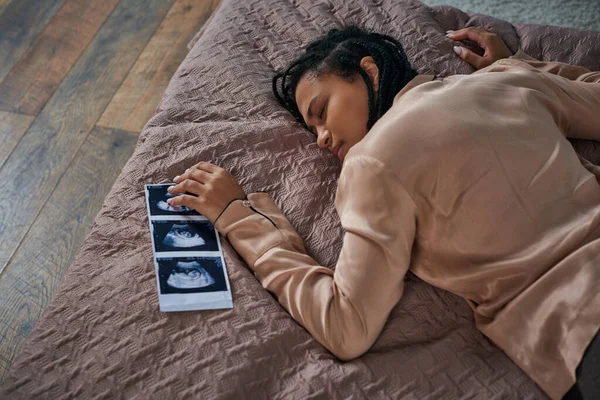 Vista superior de la mujer afroamericana preocupada acostada en la cama cerca de ultrasonido, bebé nonato, aborto - foto de stock