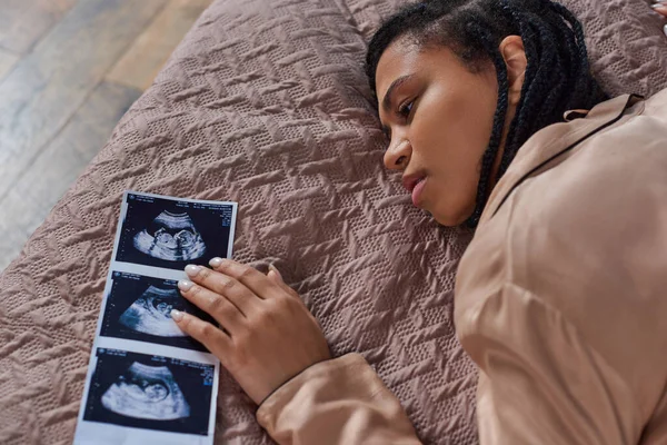Draufsicht auf besorgte Afroamerikanerin, die in der Nähe von Ultraschall auf dem Bett liegt, Abtreibungskonzept — Stockfoto