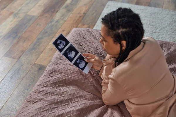 Top view of african american woman lying on bed, looking at ultrasound, abortion concept, stress — Stock Photo