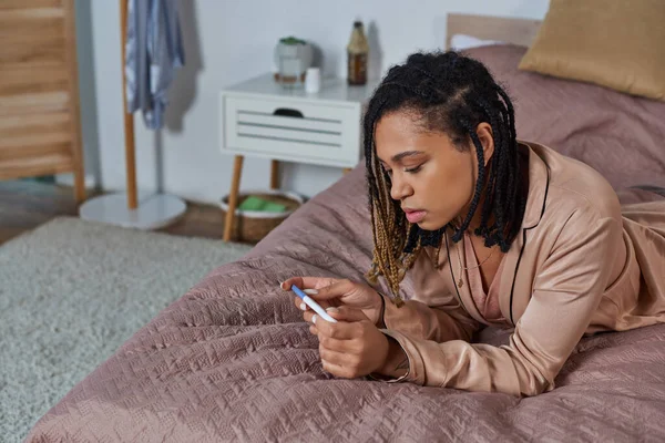 African american woman lying on bed, looking at pregnancy test, making decision, abortion concept — Stock Photo