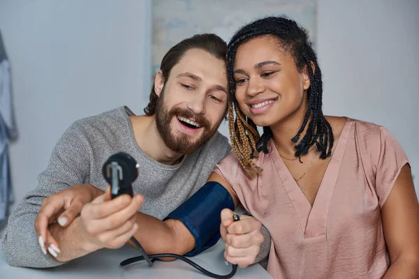 Homme joyeux mesurant la pression artérielle de la femme afro-américaine enceinte, futurs parents, bonheur — Photo de stock