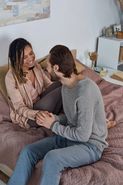 Futuri genitori, felicità, uomo gioioso che tiene per mano la moglie africana americana incinta in camera da letto — Foto stock