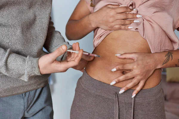Cropped man making hormonal injections in belly of african american wife, tattoo, fertility concept — Stock Photo