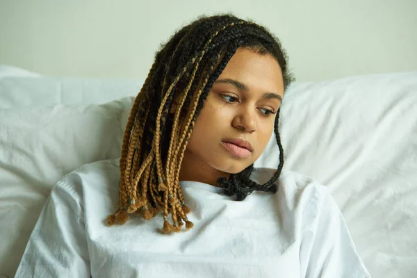 Desesperación, triste mujer afroamericana acostada en una sala privada, hospital, concepto de aborto involuntario, mirar hacia otro lado - foto de stock