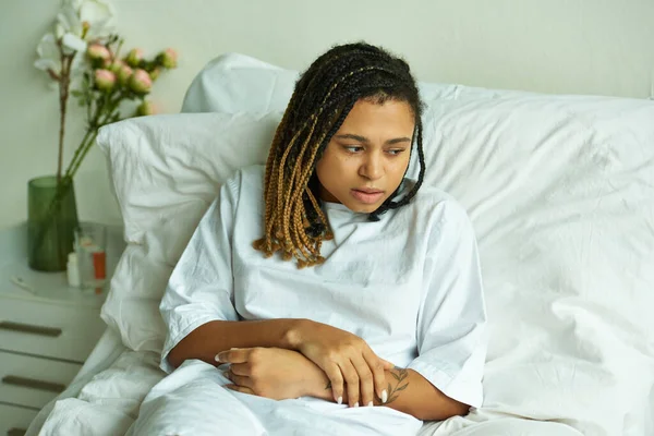 Donna afroamericana sconvolta sdraiata in reparto privato, fiori, bicchiere d'acqua, ospedale, aborto spontaneo — Foto stock