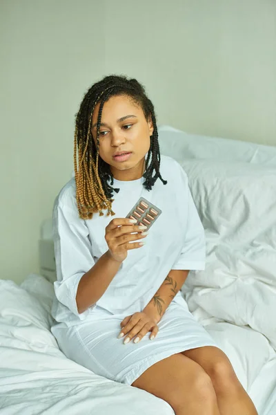 African american woman sitting on bed,  private ward, hospital, holding pills, miscarriage concept — Stock Photo
