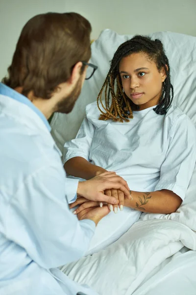 Doctor en bata blanca cogido de la mano de la mujer afroamericana, reconfortante, sala privada, aborto espontáneo - foto de stock