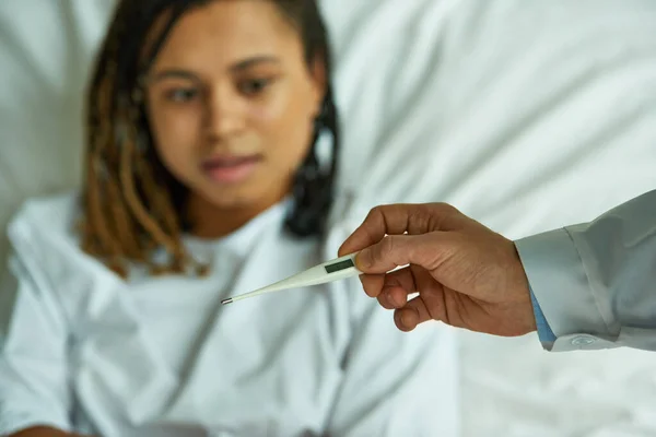 Doctor holding thermometer near african american woman, private ward, hospital, symptoms, disease — Stock Photo