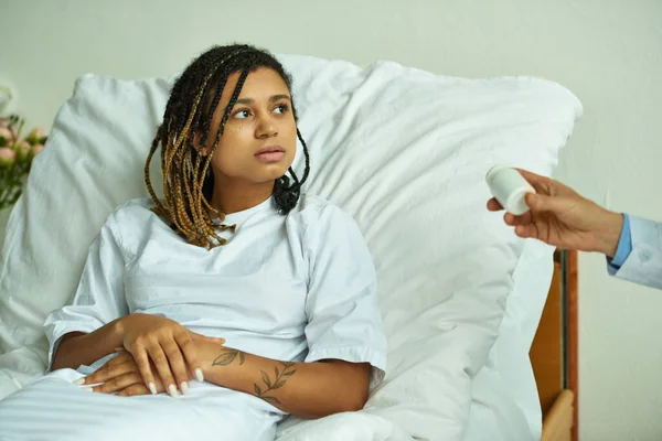 Doctor holding bottle with pills near sad african american woman, private ward, consultation — Stock Photo