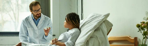 Doctor holding bottle with pills near african american woman, ward, prescribing medication, banner — Stock Photo