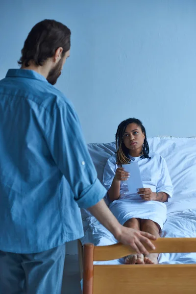 Husband standing near private ward of sad african american wife, hospital, miscarriage concept — Stock Photo