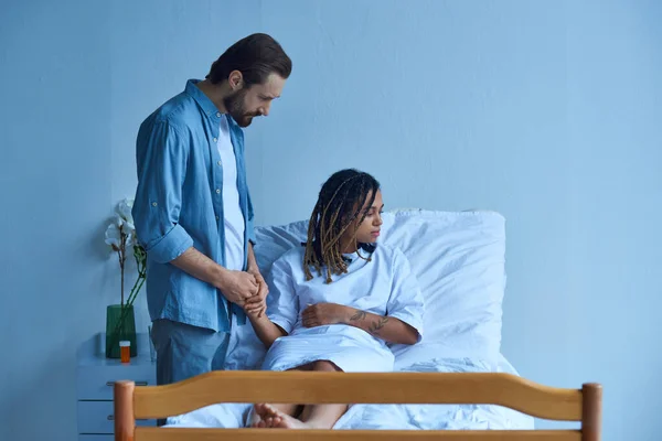 Концепция выкидыша, мужчина держит за руку африканскую американскую жену, утешает, больничный пациент — стоковое фото