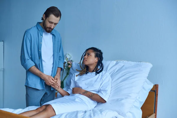 Концепція викидня, чоловік тримає руку пригніченої афроамериканської дружини, лікарні, приватної палати — стокове фото