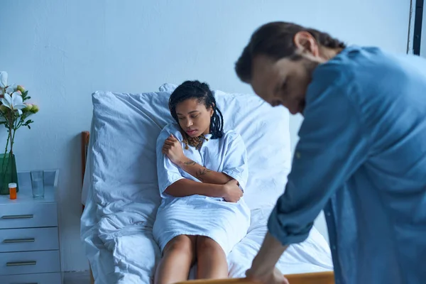 Concept fausse couche, femme afro-américaine déprimée couchée dans un lit d'hôpital près du mari, chagrin — Photo de stock