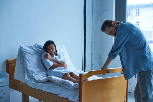 Conceito de aborto espontâneo, mulher afro-americana deprimida deitada na cama do hospital perto do marido, desespero — Fotografia de Stock