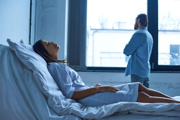 Conceito de aborto espontâneo, mulher afro-americana deprimida de luto, deitada na cama do hospital perto do marido — Fotografia de Stock