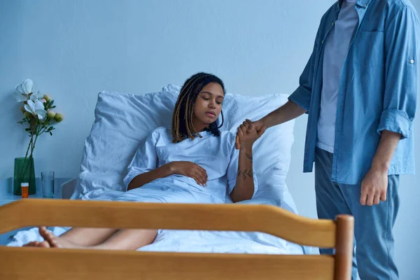 Aborto espontâneo, homem chateado segurando a mão da triste esposa afro-americana, dor, cama de hospital, enfermaria privada — Fotografia de Stock