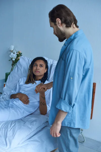 Fausse couche, homme tenant la main d'une femme afro-américaine déprimée, deuil, lit d'hôpital, salle privée — Photo de stock