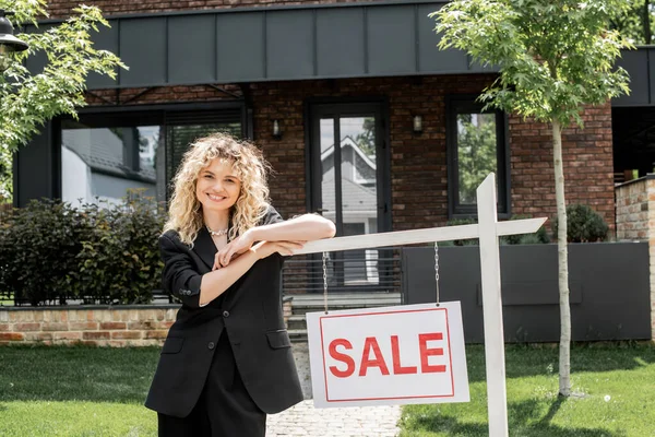 Gai agent immobilier blonde debout à proximité à vendre enseigne à côté de chalet — Photo de stock