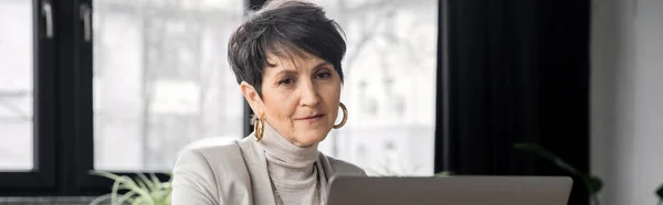 Впевнена жінка середнього віку, корпоративний менеджер, що працює на ноутбуці в офісі, банер — стокове фото