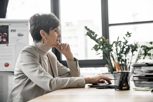 Seitenansicht der nachdenklichen Geschäftsfrau, die im modernen Büro am Laptop arbeitet, kreatives Denken — Stockfoto