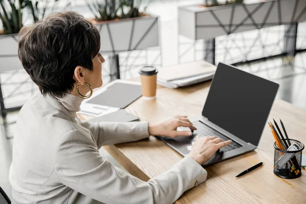 Reife Geschäftsfrau arbeitet am Laptop in der Nähe von Dokumenten und Kaffee am Arbeitsplatz im modernen Büro — Stockfoto