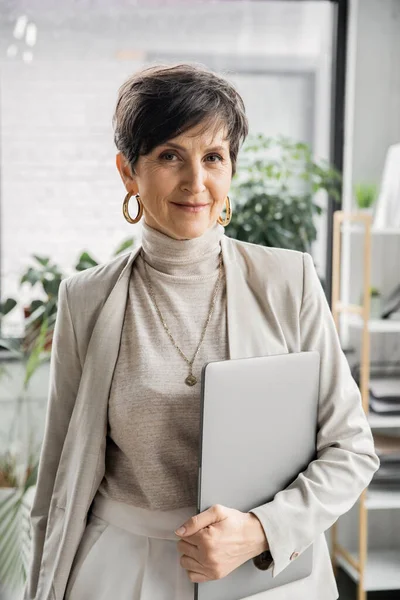 Heureuse femme d'affaires mature avec ordinateur portable regardant la caméra dans le bureau, portrait, headshot professionnel — Photo de stock
