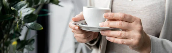 Обрізаний вид середнього віку підприємця з чашкою кави, що стоїть в офісі, банер — стокове фото