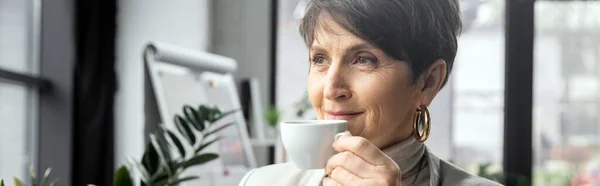Pleased mature woman, executive manager, drinking coffee and looking away in modern office, banner — Stock Photo
