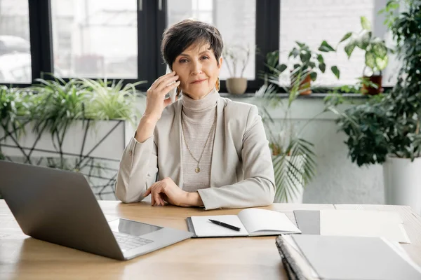 Smiling mature businesswoman looking at camera in office, laptop, notebook, professional headshot — Stock Photo