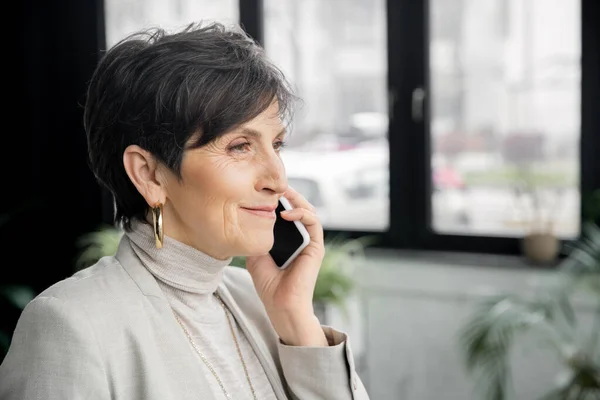 Glückliche und stilvolle Geschäftsfrau mittleren Alters, die im modernen Arbeitsumfeld mit dem Handy telefoniert — Stockfoto